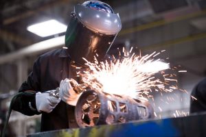 Person wearing a welding mask and gloves, actively welding with sparks flying