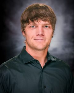 Headshot of a male with golden shaggy hair, blue eyes, and a black collared shirt