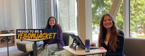 Two RCTC students sit at separate study tables near each other with open laptops. On one of the study tables is a navy-blue sign, "Proud to be a Yellowjacket"