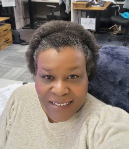 Woman wearing a beige sweater and short curly black and grey hair pulled back with a headband
